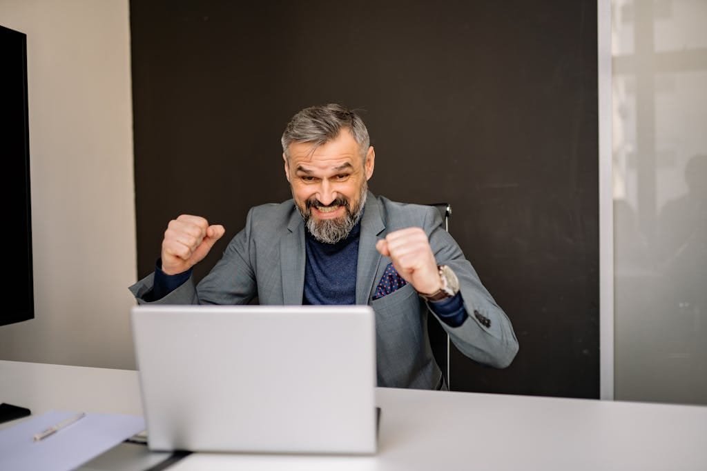 Happy businessman celebrating success while looking at laptop in modern office.